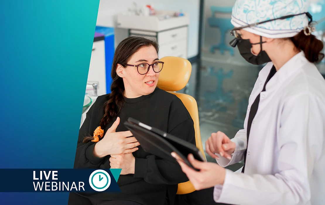 Female dental patient looking up at a dental professional in scrubs holding a tablet